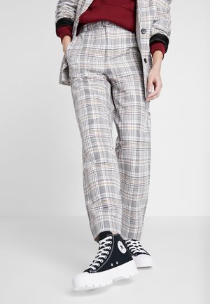 Pantalones de cuadros grises con un corte ajustado, que cuentan con bolsillos y una textura suave. Combinados con zapatillas de alta caña negras y suelas de goma blancas.