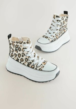 Een paar hoge sneakers met dikke witte zolen en bovenwerk van luipaardprint stof, witte veters en zwarte trekkoorden op een lichte achtergrond.
