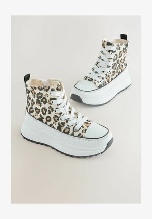 Kürkideopardimustriga kõrge säärega tossud paksude valgete talladega, valged paelad ja mustad tõmblukud heleltaustal.