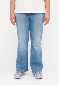 Vaaleansiniset denim-farkut, joissa on leveä lahje ja haalistunut ulkonäkö. Farkuissa on klassinen viiden taskun muotoilu ja hieman venyvyyttä mukavuutta varten.