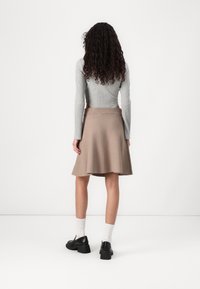 Jupe évasée beige en tissu doux, avec une texture lisse et une large ceinture. Associée à un haut gris côtelé ajusté et des chaussures noires.