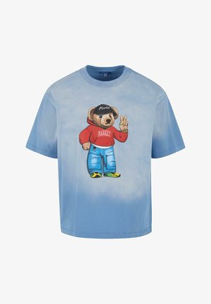 Blauwe tie-dye korte mouwen t-shirt met een berenafbeelding in een rode hoodie en blauwe spijkerbroek, met een zwarte pet en een vredesteken gebaar.