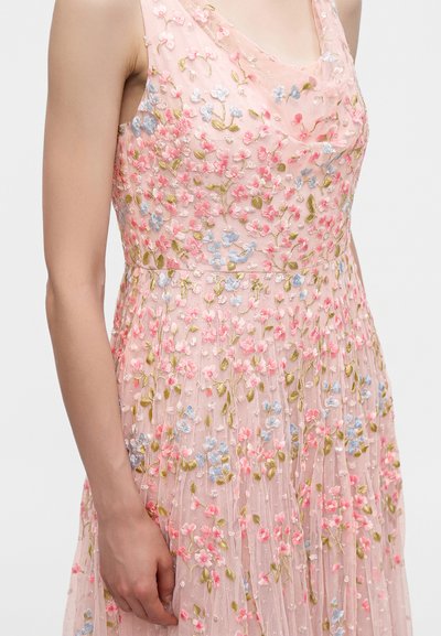 Robe rose sans manches avec une broderie florale détaillée en rose, bleu et vert, portée par une personne avec le bras relâché sur le côté.