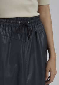 Jupe en simili cuir bleu marine avec une taille élastique et un cordon de serrage. Présente une texture lisse et deux coutures latérales discrètes.