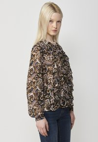 Blusa nera con stampa paisley in tonalità di marrone, rosa e blu; presenta ruches e maniche lunghe e gatherate. Indossata con jeans blu.
