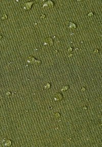 Gestructureerde groene stof met een ribbelpatroon, voorzien van waterdruppels van verschillende grootte op het oppervlak, wat duidt op waterbestendigheid.