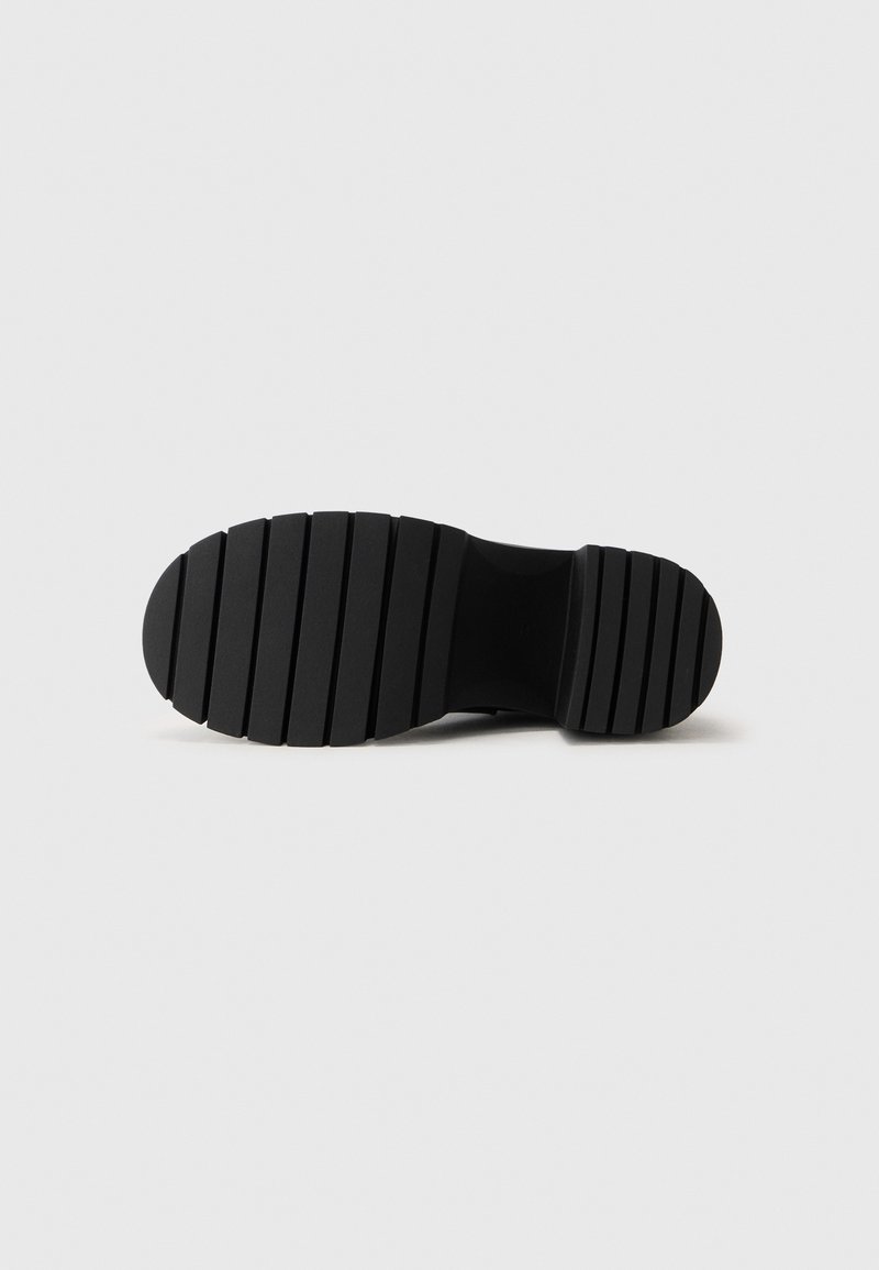 Suola di scarpa in gomma nera con scanalature orizzontali, caratterizzata da un design a punta arrotondata e una superficie testurizzata per aderenza e trazione.