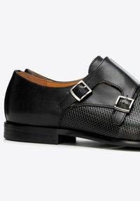 Czarny skórzany elegancki but z podwójnymi srebrnymi sprzączkami, z przodu o splatanej fakturze, a na pięcie i bokach gładki.