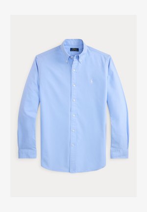 Chemise bleu clair à manches longues avec col boutonné, boutons blancs et petit logo blanc brodé sur la poitrine gauche.