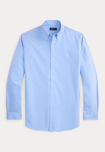 Chemise bleu clair à manches longues avec col boutonné, boutons blancs et petit logo blanc brodé sur la poitrine gauche.