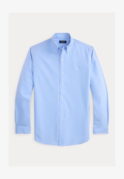Chemise bleu clair à manches longues avec col boutonné, boutons blancs et petit logo blanc brodé sur la poitrine gauche.