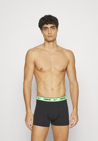 Schwarze Boxershorts mit einem leuchtend grünen Nike-Logo-Gummi; der Stoff wirkt weich und dehnbar, taillierte Passform und mittellange Beine.