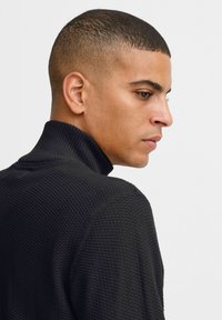 Schwarzer, gestrickter Rollkragenpullover mit strukturiertem Muster und geripptem Kragen. Die Passform ist körpernah und das Design ist schick.