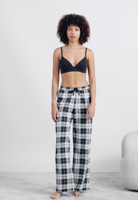 Sutiã preto e calças de pijama largas, com padrão xadrez preto e branco, cintura elástica e detalhe de atar. Tecido suave, design descontraído.