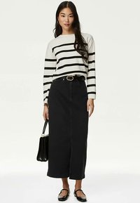 Falda larga de mezclilla negra, top de manga larga a rayas en crema y negro, y zapatos planos negros. Accesorios incluyen un bolso negro y un cinturón dorado.