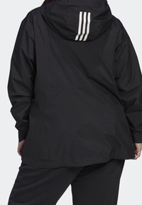 Veste noire légère avec capuche, dotée de trois rayures blanches verticales dans le dos, à manches longues et au design décontracté.