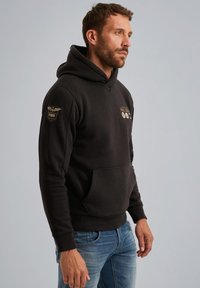 Zwarte hoodie met een trekkoord, voorzak en geborduurde patches op de mouwen. Zachte stof, slim fit ontwerp en ribgebreide manchetten.