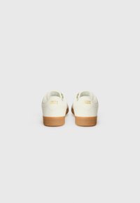 White leather sneakers with a tan rubber sole, featuring a rounded shape and embossed logo at the back. Smooth texture with minimal design.