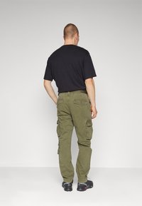 Cargo-Hosen aus olivgrünem Baumwollmischgewebe mit mehreren Seitentaschen, einem lässigen Schnitt und geradem Bein, kombiniert mit einem schwarzen T-Shirt.