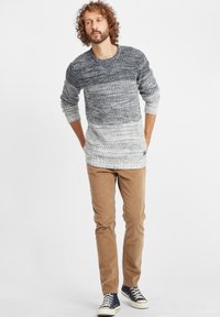 Strickpullover in einem Verlauf von Marineblau zu Weiß, langärmelig, mit gerippten Bündchen; kombiniert mit hellbraunen Cordhosen und marineblauen Sneakers.