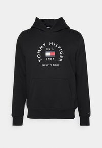 Sudadera negra con capucha y bolsillo frontal, que presenta el texto blanco "TOMMY HILFIGER EST. 1985 NEW YORK" y el logo de la bandera en rojo, blanco y azul.