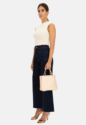 Top bianco a righe senza maniche, jeans a gamba larga in denim scuro a vita alta, sandali con tacco a strappo dorati e una borsa strutturata di colore rosa chiaro.