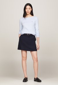 Maglione azzurro chiaro a maniche lunghe, gonna a ruota blu navy con pieghe frontali e mocassini neri. Design semplice senza motivi, con una cintura.