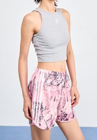 Top cropped senza maniche grigio con logo bianco, abbinato a pantaloni corti con motivo camouflage rosa, dotati di strisce laterali bianche e una vita elastica.