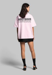 Růžové oversized tričko s černým textem na zádech. Krátké rukávy, kulatý výstřih a rovný lem. Nosit s černou mini sukní a ponožkami.