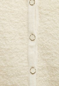 Tissu texturé écru avec une rangée verticale de boutons ronds de couleur crème bordés d'or.