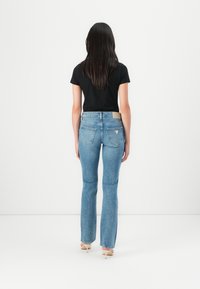 Blue denim flared jeans with a mid-rise waist, back pockets, and a tan leather patch on the waistband. Worn with a fitted black top.