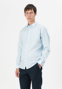 Helles blaues Langarmhemd mit Button-Down-Kragen, vorderen Knöpfen und Manschetten; kombiniert mit dunkelblauen Hosen; glatte Stoffoberfläche.