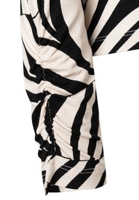 Black and beige striped garment detail featuring gathered texture on the sleeve, with a soft, lightweight fabric and visible stitching.