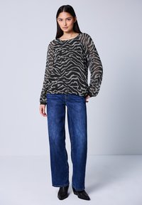 Top lungo a maniche nere e grigie con motivi a zebra abbinato a jeans blu dritti e stivaletti neri.