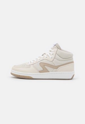 Hooge sneaker in beige en tan leer met witte veters en een dikke witte zool op een effen achtergrond.
