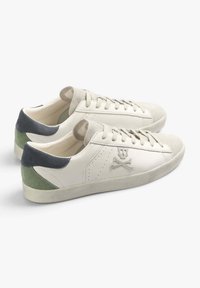Sneakers bianchi in pelle con tallone in suede verde e grigio, dettagli perforati e logo con teschio e ossa incrociate sul lato. Suola in gomma.
