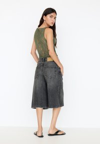 Green lace sleeveless top paired with loose black denim culottes. The culottes feature a frayed hem and two back pockets. Flat black sandals.