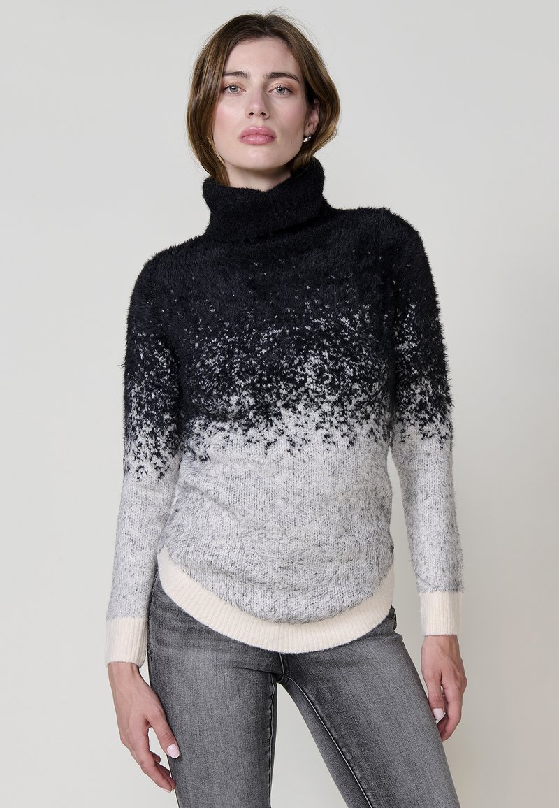 Črno-sivo ombre turtleneck pulover iz mehkega, puhastnega materiala z rebrastimi manšetami in ukrivljenim robom. Obut je z sivimi kavbojkami.