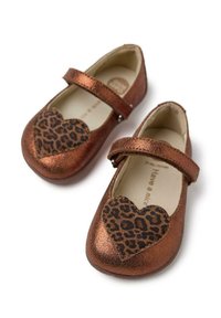 Bailarinas sintéticas de bronce con un parche de leopardo en forma de corazón, sujetas por una correa en el empeine. Suelas planas, punteras redondeadas, textura suave.