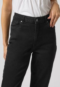 Jeans neri a vita alta realizzati in denim. Presentano cinque tasche, chiusura con bottone e zip, e un design a gamba dritta con una texture morbida.