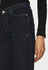 Mörk denimjeans med gul sömnad, sidofickor och en figurnära design. Tyget har en mjuk textur med lätt stretch.