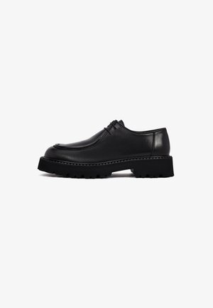 Zapatos de cuero negro con punta redondeada, parte superior texturizada y suela de goma gruesa y estriada. Presentan un cordón mínimo y un acabado suave.