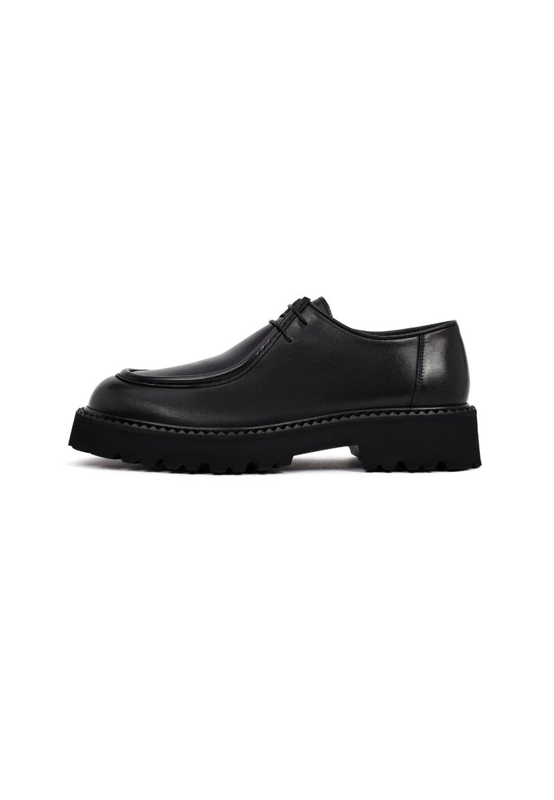Zapatos de cuero negro con punta redondeada, parte superior texturizada y suela de goma gruesa y estriada. Presentan un cordón mínimo y un acabado suave.
