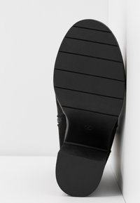 Zapato negro de tacón con un upper texturizado y una suela de goma. Presenta una superficie suave con surcos horizontales para mayor agarre.