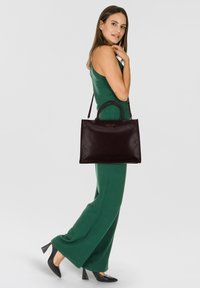 Sac à main en cuir noir avec deux poignées arrondies et un fond plat. Le sac présente un discret logo sur le devant et une texture lisse.
