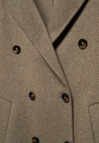 Manteau croisé en laine marron avec de larges revers et six boutons foncés en écaille disposés en deux colonnes.