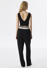 Zwart geribbeld crop top met een diepe V-uitsnijding aan de achterkant, gecombineerd met zwarte wijde broek met een witte elastische tailleband met het label "LA CRÈME."