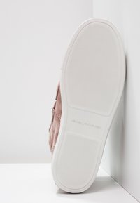 Sneaker in suede rosa con suola in gomma bianca, fondo testurizzato e logo impresso sul tallone. L'immagine si concentra sulla parte inferiore della scarpa.