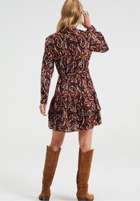 Abito marrone con motivo paisley, maniche lunghe, vita svasata e orlo a ruffles a strati, abbinato a stivali in suede color cammello al ginocchio.