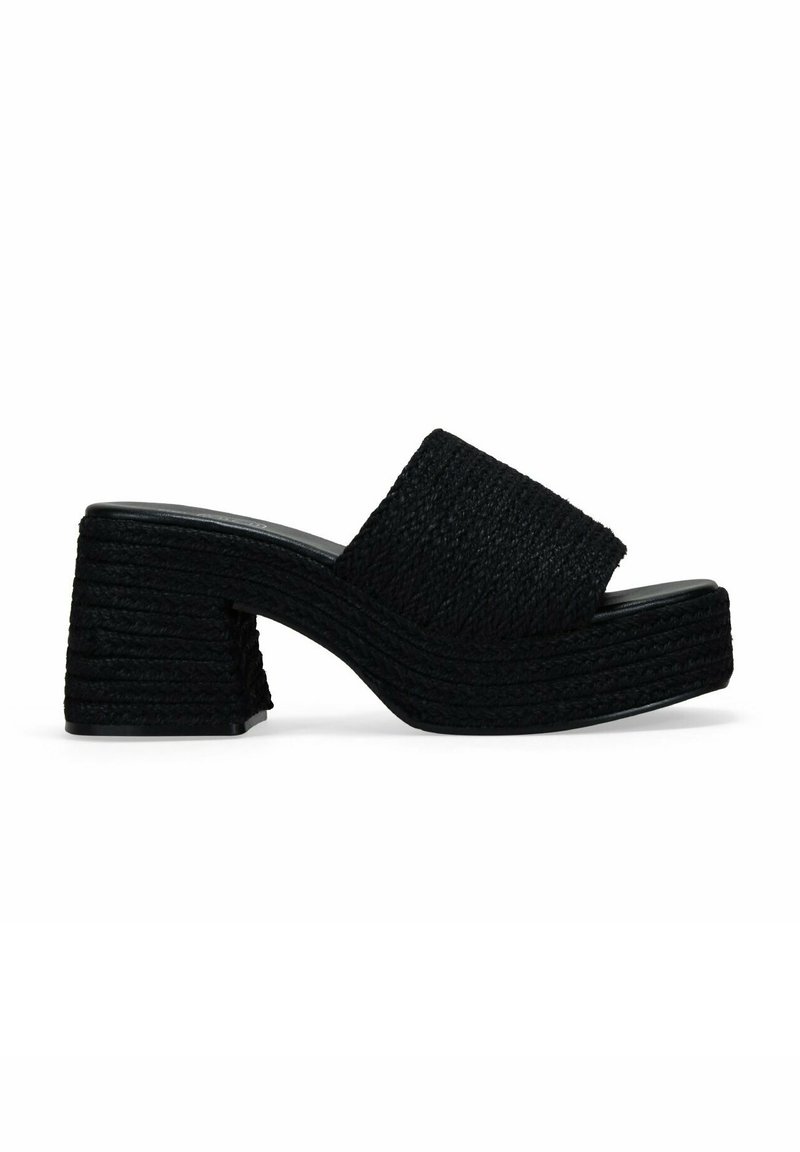 Mules negros de cuña con un upper de tejido texturizado y trenzado y un tacón grueso y estriado. Cuenta con una tira ancha en el empeine para mayor soporte.